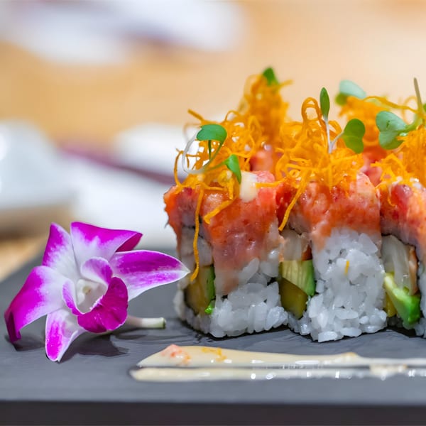 Asuka Japanese Cuisine's sushi rolls topped with salmon, crispy orange strands, and microgreens, with an orchid.