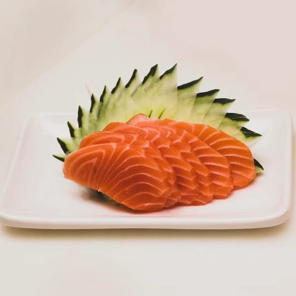 Asuka Japanese Cuisine's salmon sashimi, neatly arranged with decorative cucumber slices on a white plate.