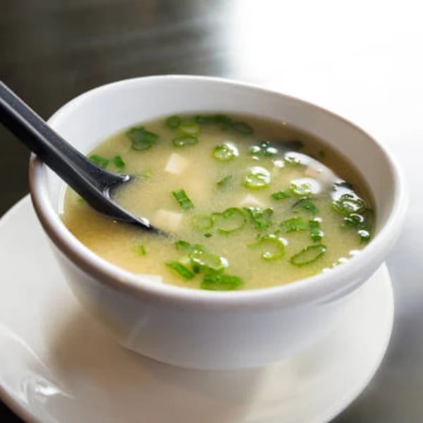 A white bowl of Asuka Japanese Cuisine miso soup with tofu and green onions.